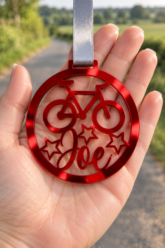 red mirror acrylic personalised cycling medal with custom name on a silver ribbon, held in hand in front of a blurred country road