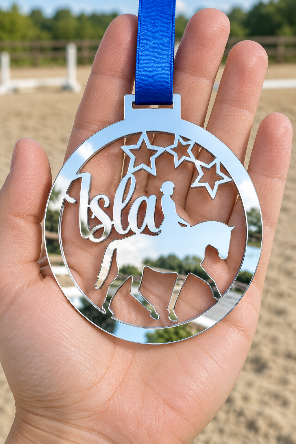 Load image into Gallery viewer, silver mirror acrylic personalised horse riding medal with custom name on a blue ribbon, held in hand in front of a blurred riding arena
