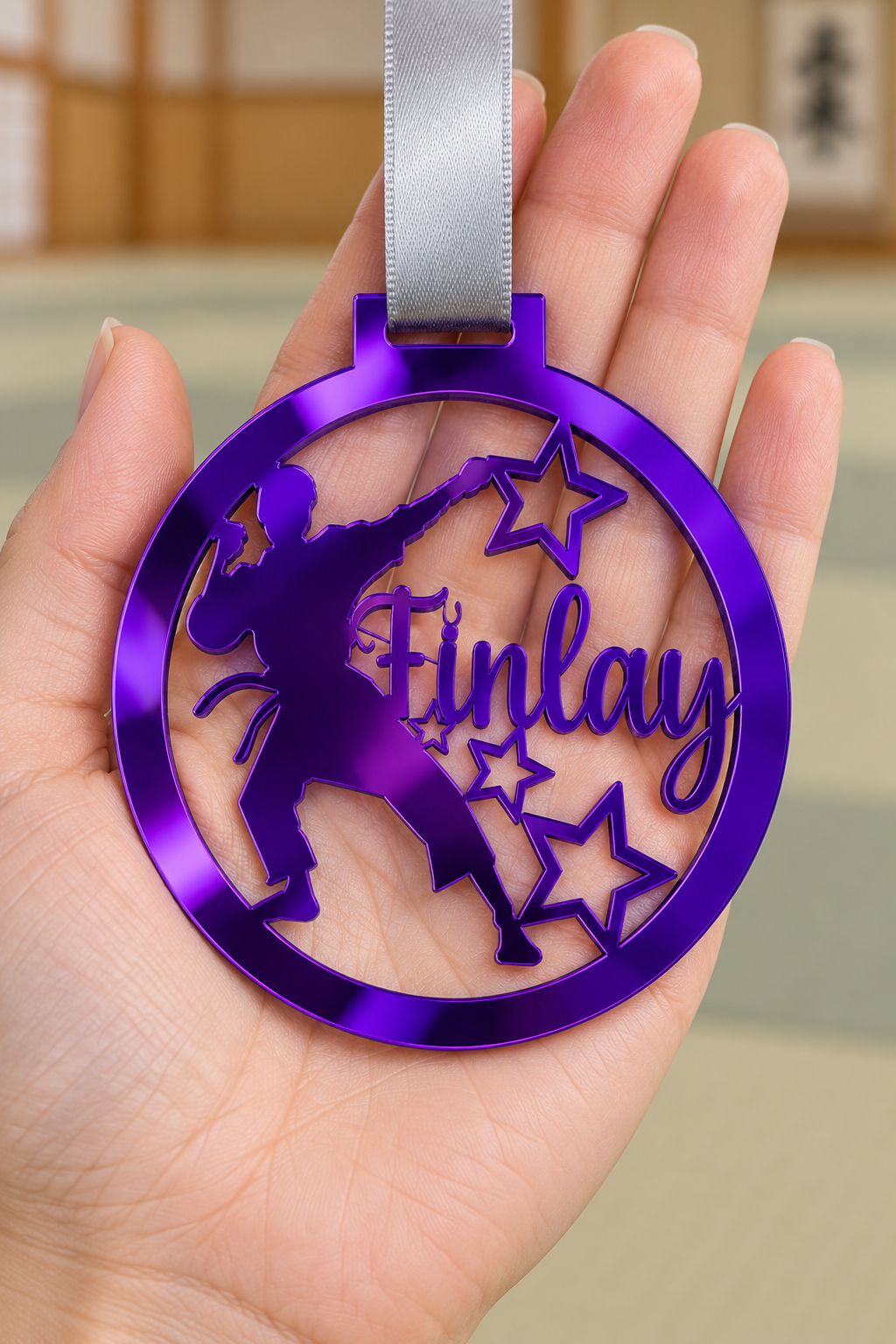 Load image into Gallery viewer, purple mirror acrylic personalised karate boy medal with custom name on a silver ribbon, held in hand in front of a blurred dojo
