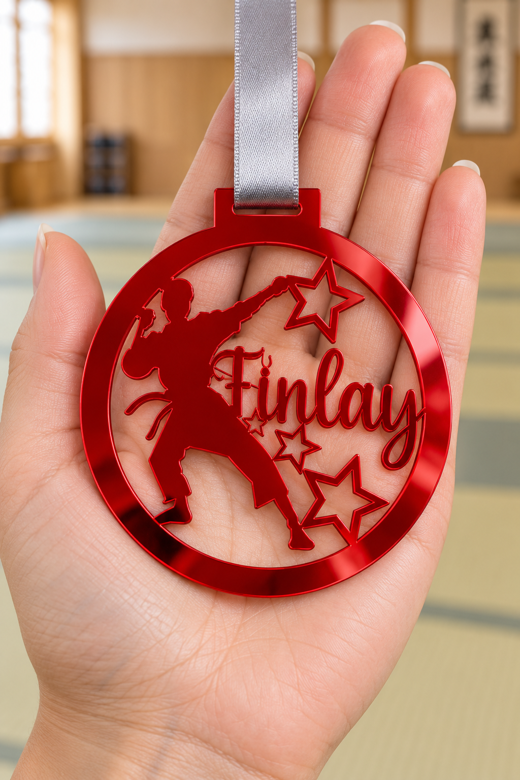 Load image into Gallery viewer, red mirror acrylic personalised karate boy medal with custom name on a silver ribbon, held in hand in front of a blurred dojo
