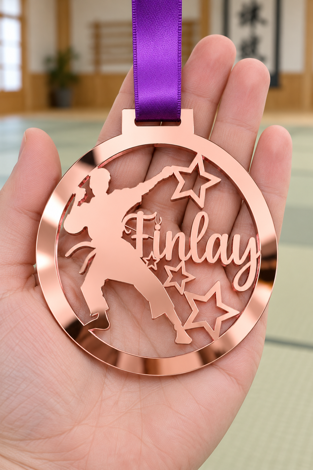 Load image into Gallery viewer, rose gold mirror acrylic personalised karate boy medal with custom name on a purple ribbon, held in hand in front of a blurred dojo
