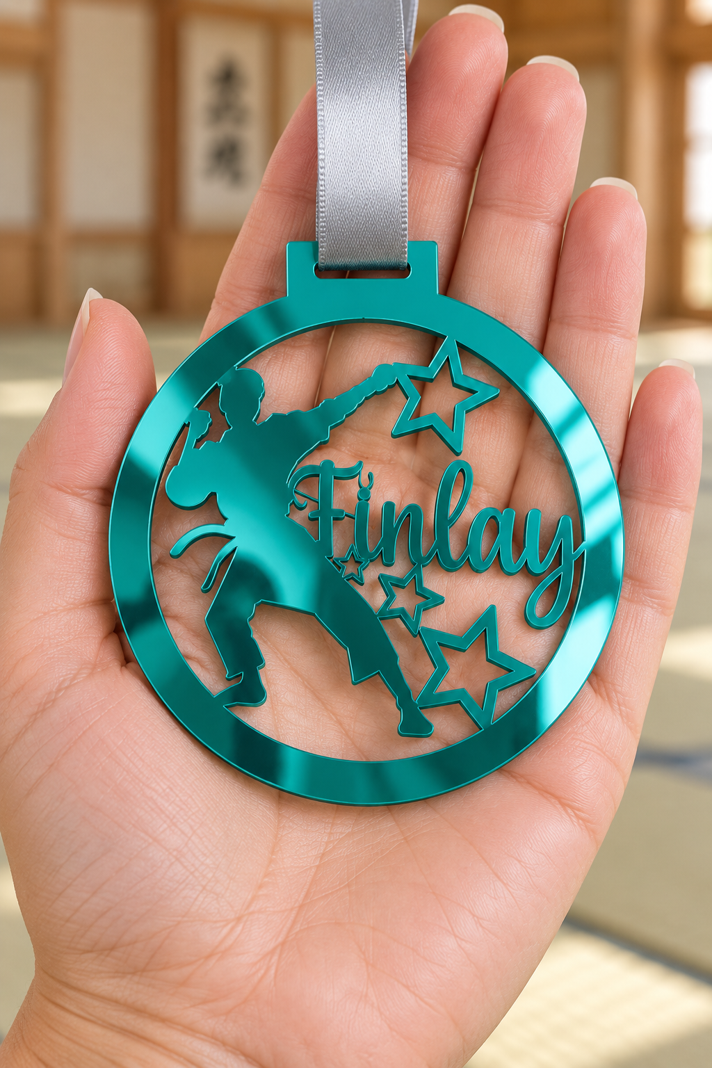 Load image into Gallery viewer, teal mirror acrylic personalised karate boy medal with custom name on a silver ribbon, held in hand in front of a blurred dojo
