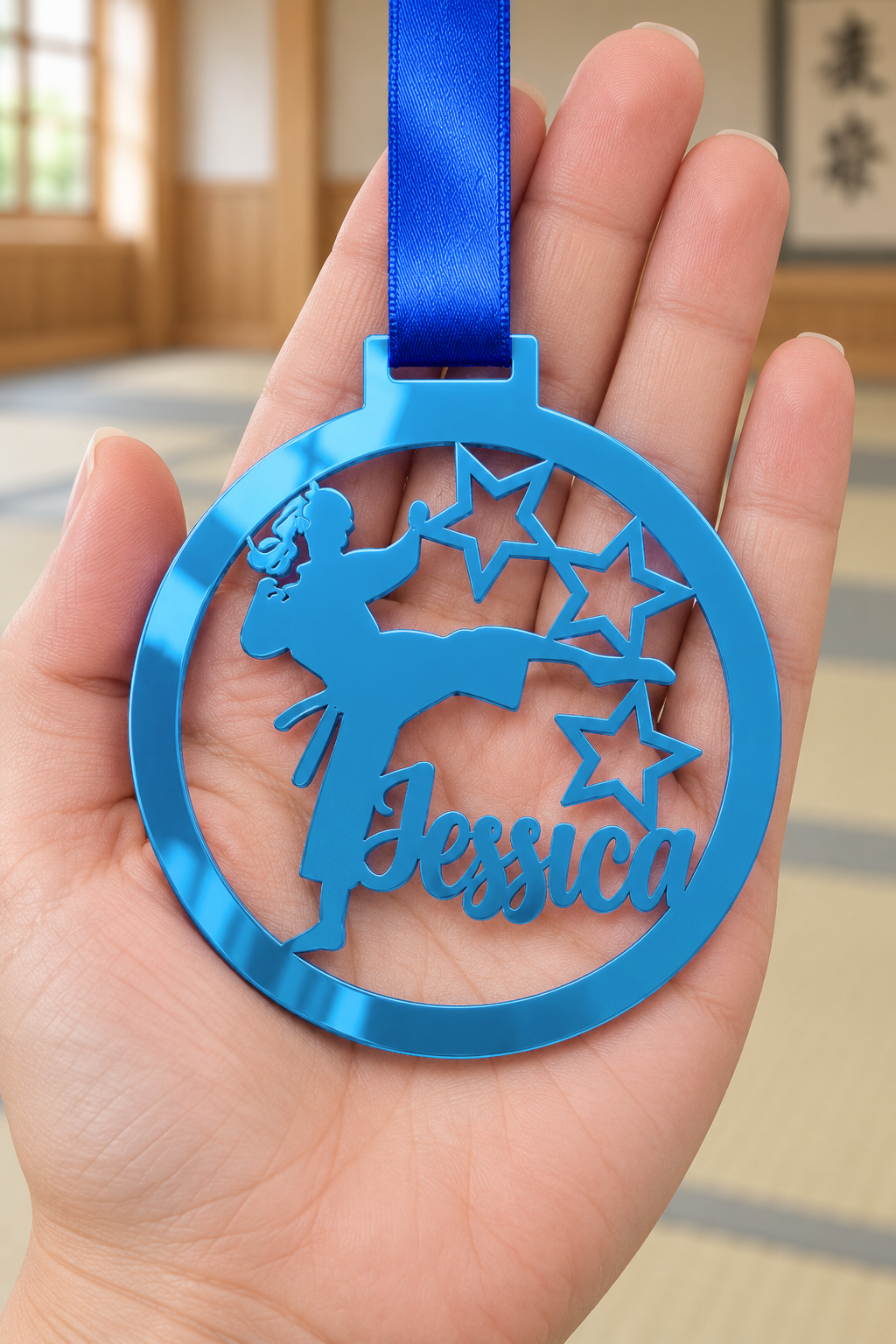 Load image into Gallery viewer, blue mirror acrylic personalised karate girl medal with custom name on a blue ribbon, held in hand in front of a blurred dojo
