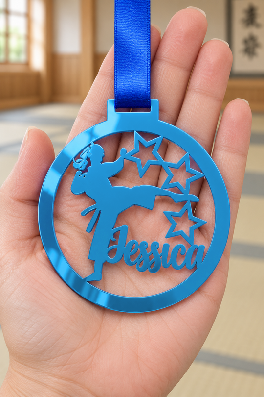 blue mirror acrylic personalised karate girl medal with custom name on a blue ribbon, held in hand in front of a blurred dojo