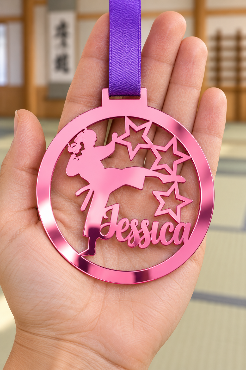Load image into Gallery viewer, pink mirror acrylic personalised karate girl medal with custom name on a purple ribbon, held in hand in front of a blurred dojo
