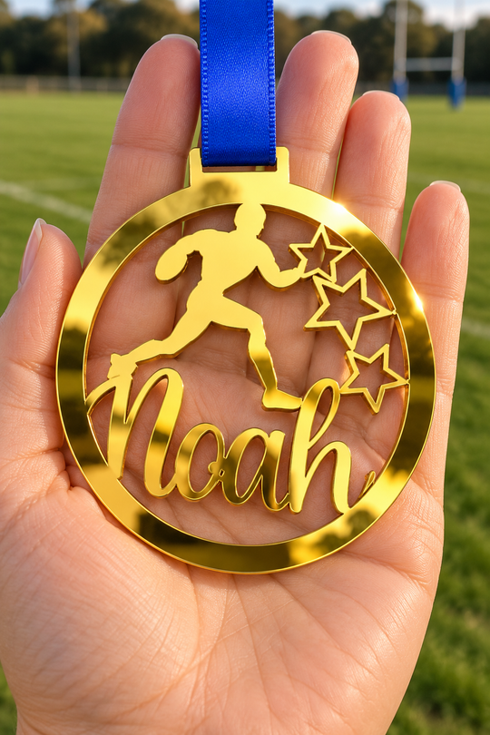 gold mirror acrylic personalised rugby medal with custom name on a blue ribbon, held in hand in front of a blurred rugby pitch