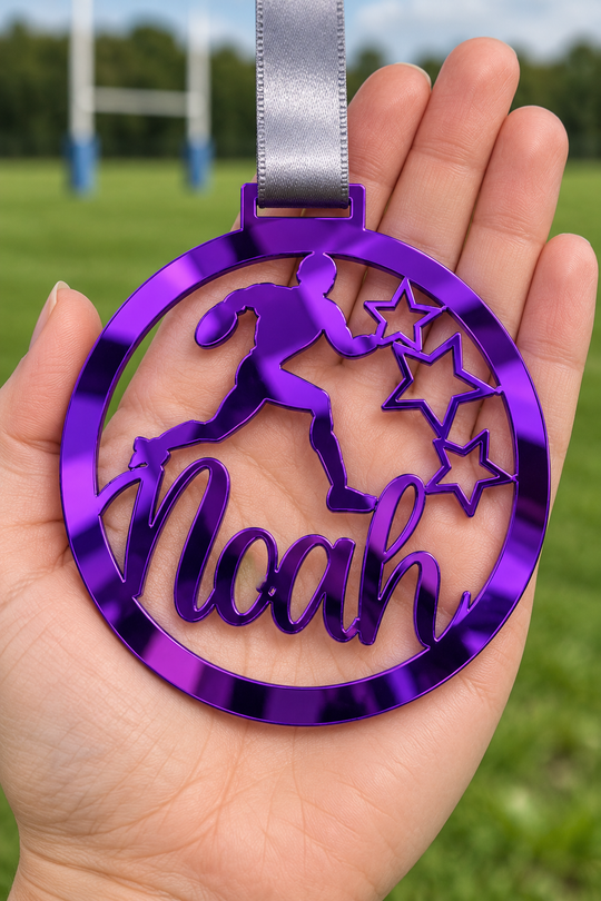 purple mirror acrylic personalised rugby medal with custom name on a silver ribbon, held in hand in front of a blurred rugby pitch
