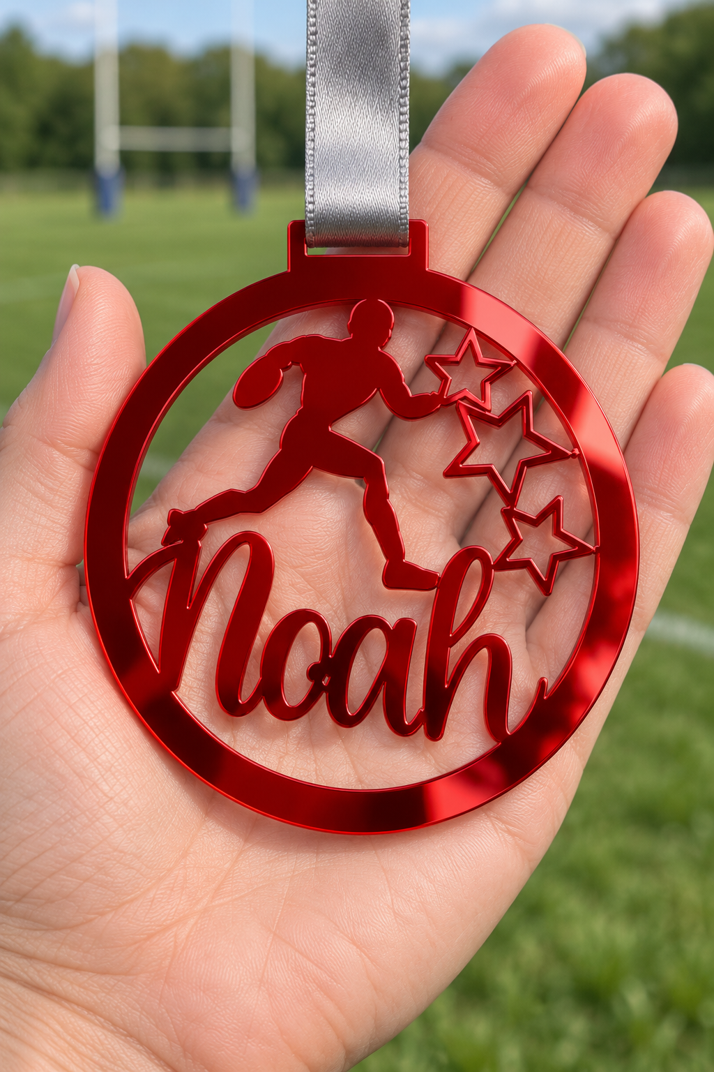 Load image into Gallery viewer, red mirror acrylic personalised rugby medal with custom name on a silver ribbon, held in hand in front of a blurred rugby pitch
