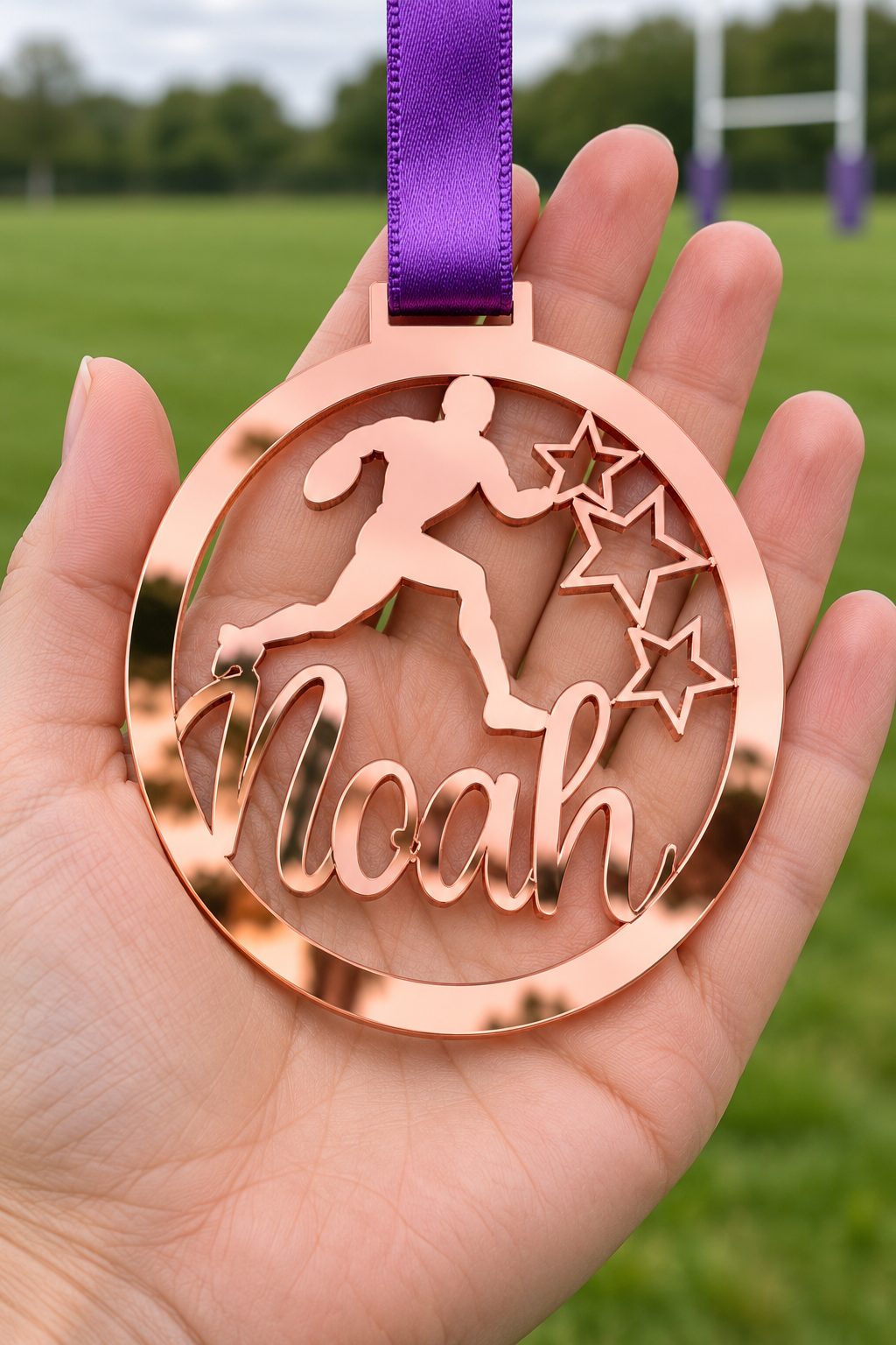 Load image into Gallery viewer, rose gold mirror acrylic personalised rugby medal with custom name on a purple ribbon, held in hand in front of a blurred rugby pitch
