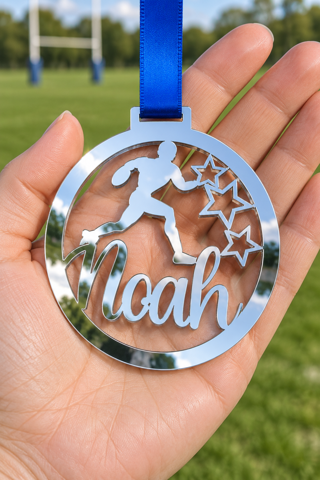 Load image into Gallery viewer, silver mirror acrylic personalised rugby medal with custom name on a blue ribbon, held in hand in front of a blurred rugby pitch
