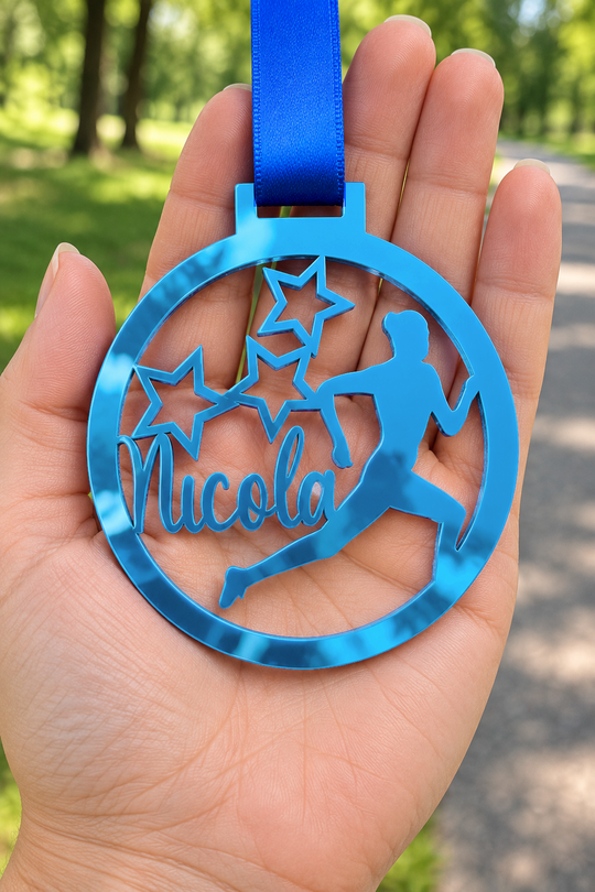blue mirror acrylic personalised running medal with custom name on a blue ribbon, held in hand in front of a blurred park running path