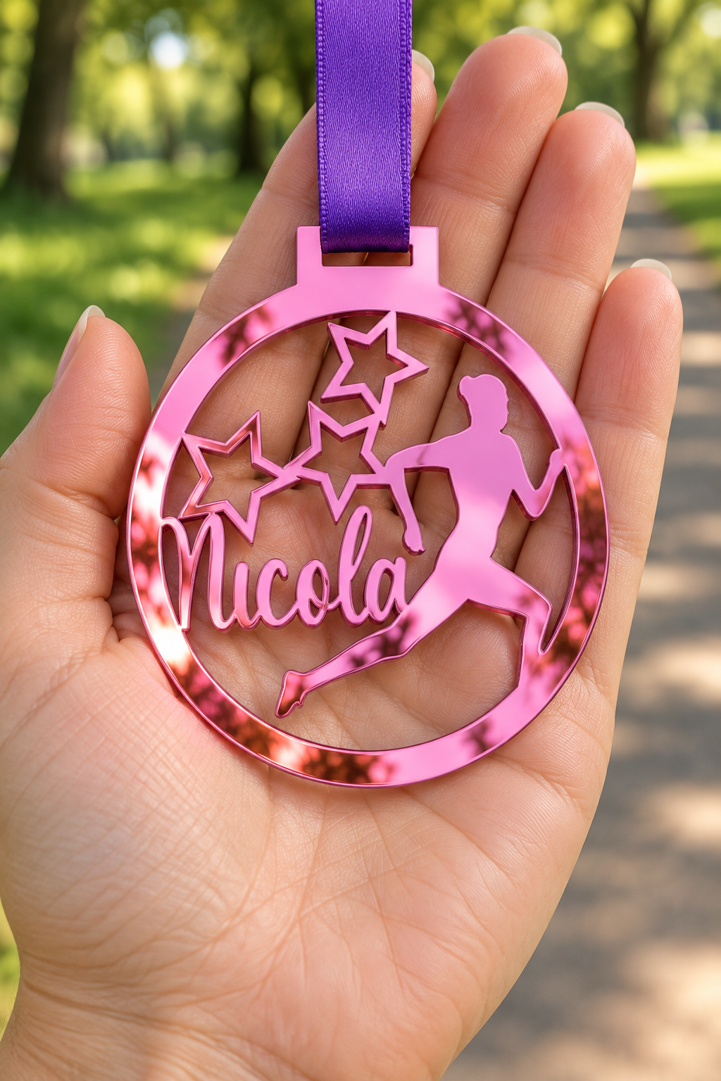 Load image into Gallery viewer, pink mirror acrylic personalised running medal with custom name on a purple ribbon, held in hand in front of a blurred park running path
