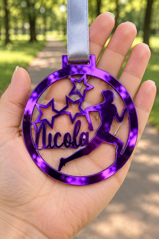 purple mirror acrylic personalised running medal with custom name on a silver ribbon, held in hand in front of a blurred park running path
