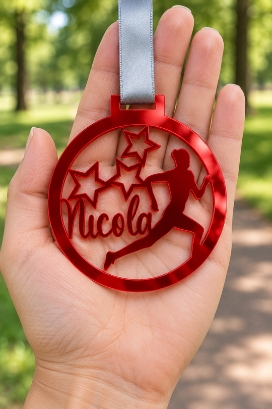red mirror acrylic personalised running medal with custom name on a silver ribbon, held in hand in front of a blurred park running path