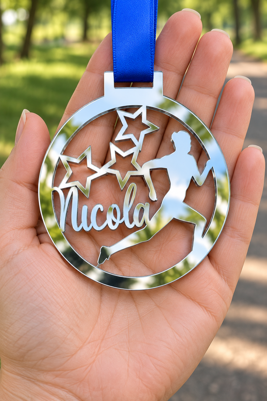 Load image into Gallery viewer, silver mirror acrylic personalised running medal with custom name on a blue ribbon, held in hand in front of a blurred park running path
