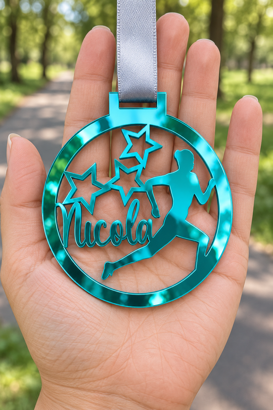 teal mirror acrylic personalised running medal with custom name on a silver ribbon, held in hand in front of a blurred park running path