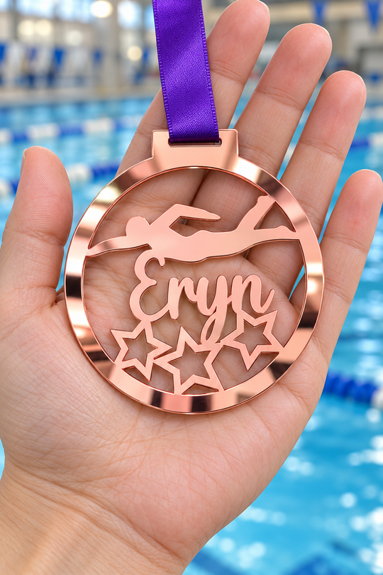rose gold mirror acrylic personalised swimming medal with custom name on a purple ribbon, held in hand in front of a blurred swimming pool