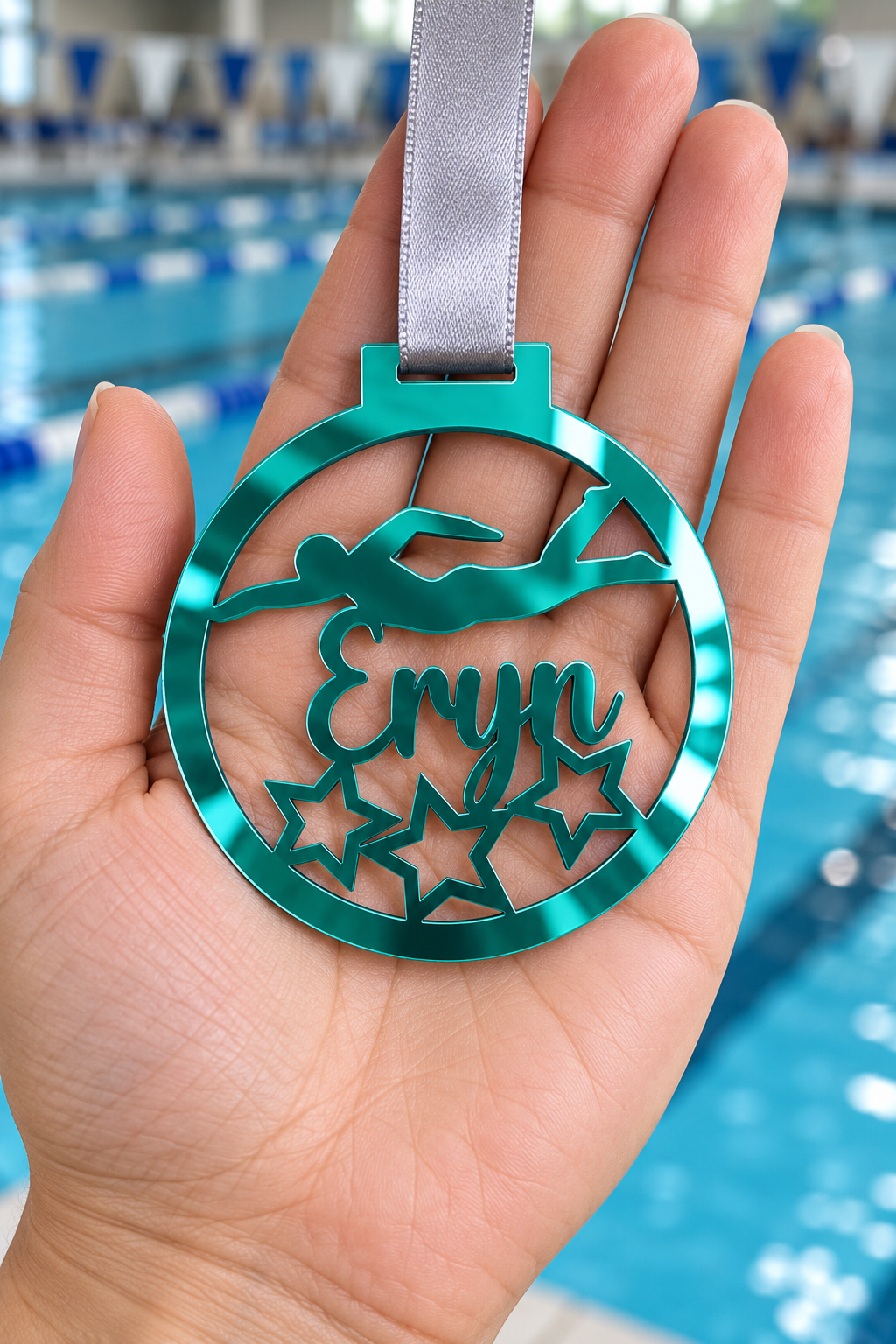 Load image into Gallery viewer, teal mirror acrylic personalised swimming medal with custom name on a silver ribbon, held in hand in front of a blurred swimming pool
