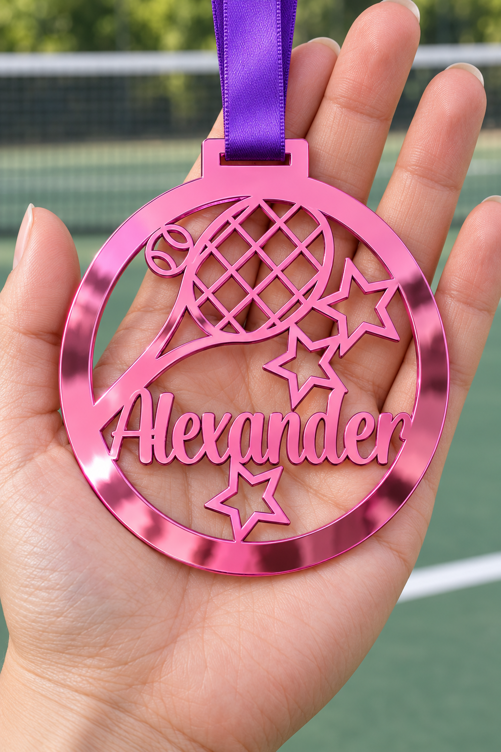 Load image into Gallery viewer, pink mirror acrylic personalised tennis medal with custom name on a purple ribbon, held in hand in front of a blurred tennis court
