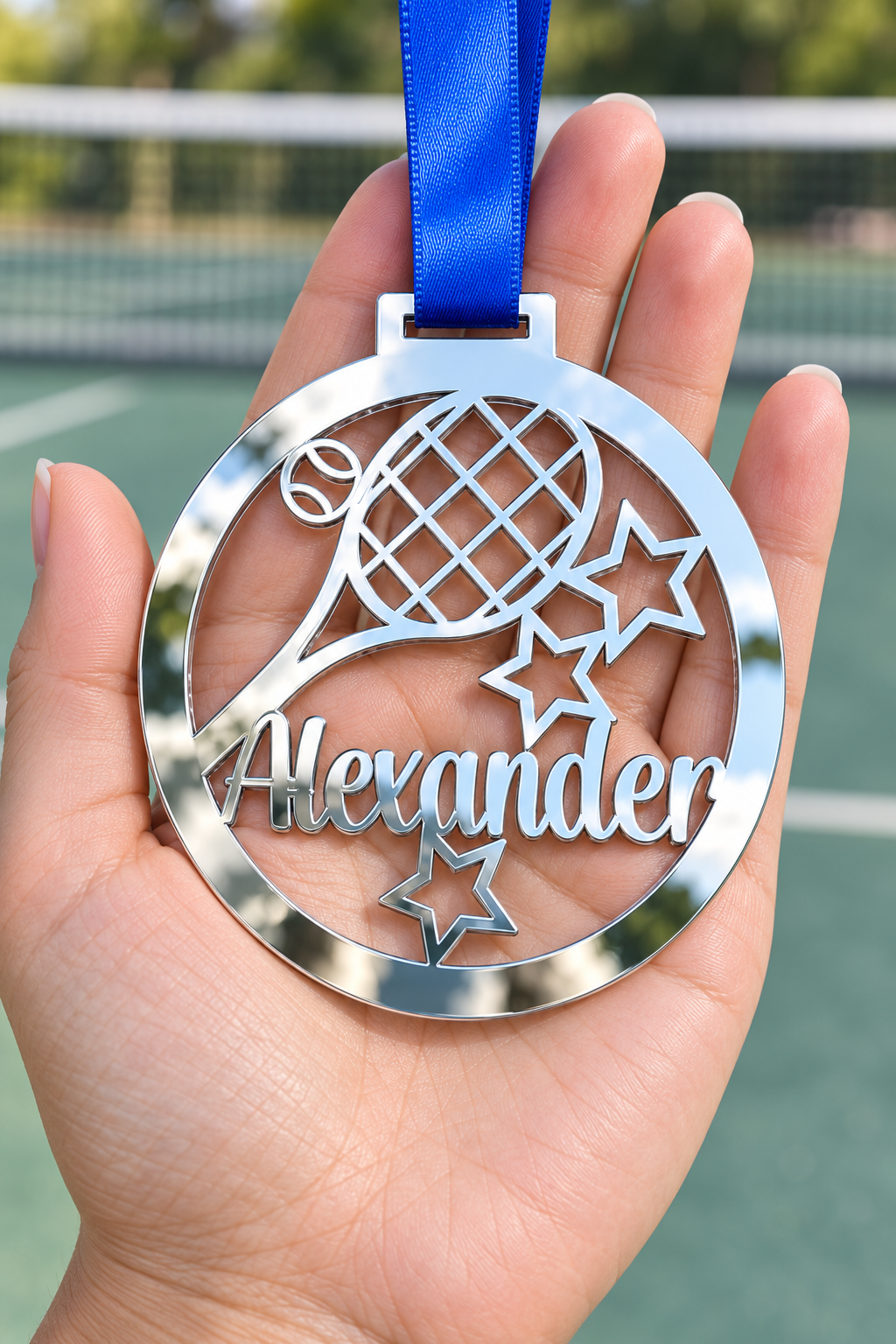 Load image into Gallery viewer, silver mirror acrylic personalised tennis medal with custom name on a blue ribbon, held in hand in front of a blurred tennis court
