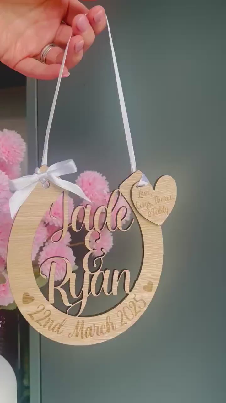 Load and play video in Gallery viewer, Personalised oak veneer wedding horseshoe with names, date, heart charm and white ribbon

