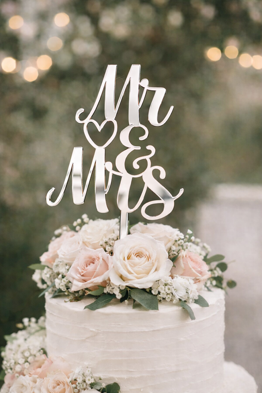 Silver mirror acrylic Mr and Mrs wedding cake topper on a white buttercream wedding cake with blush roses and greenery.