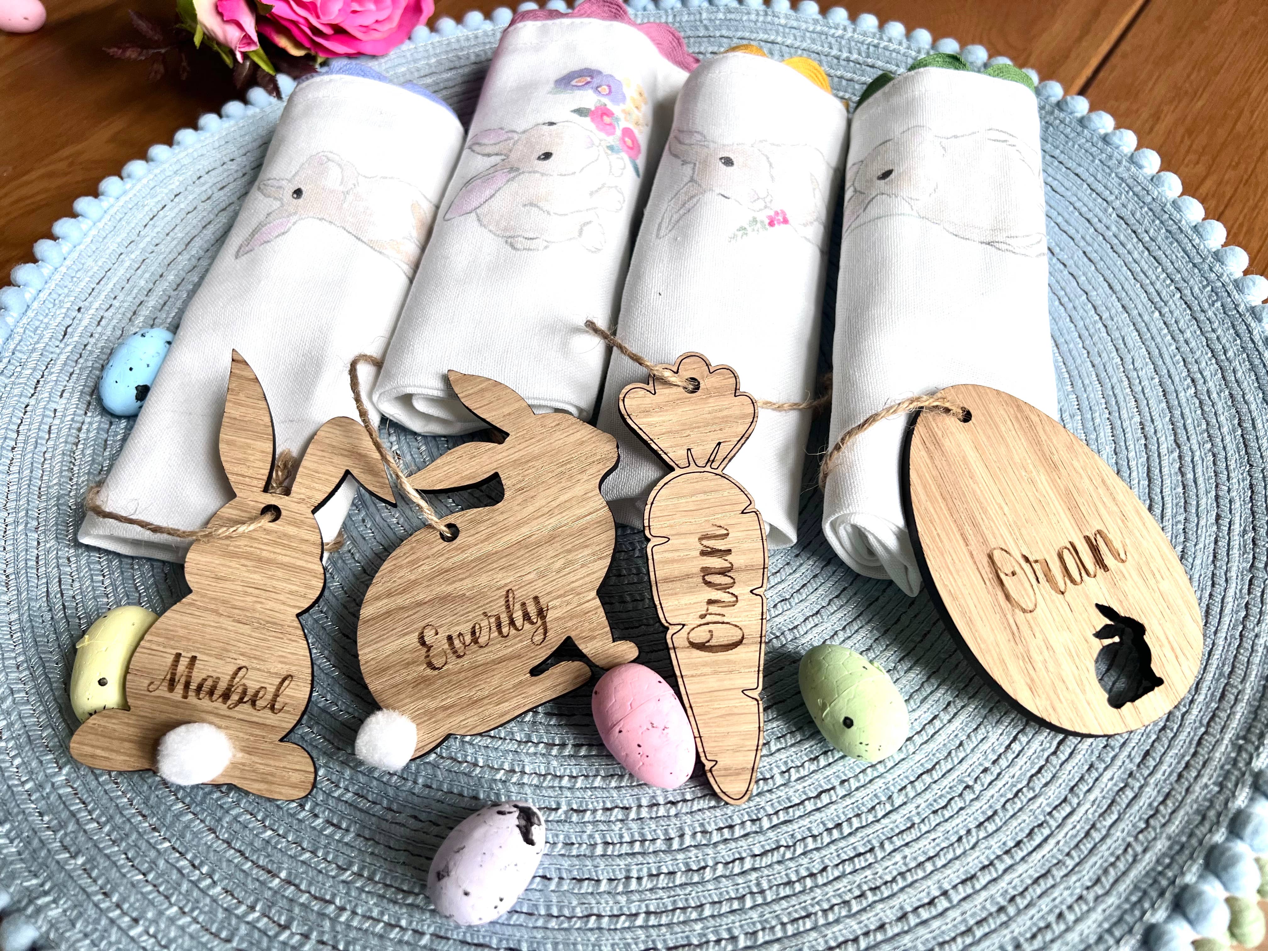 A set of four wooden hanging Easter decorations including cut-out bunny shapes and egg designs, displayed on a table with Easter eggs and fabric.