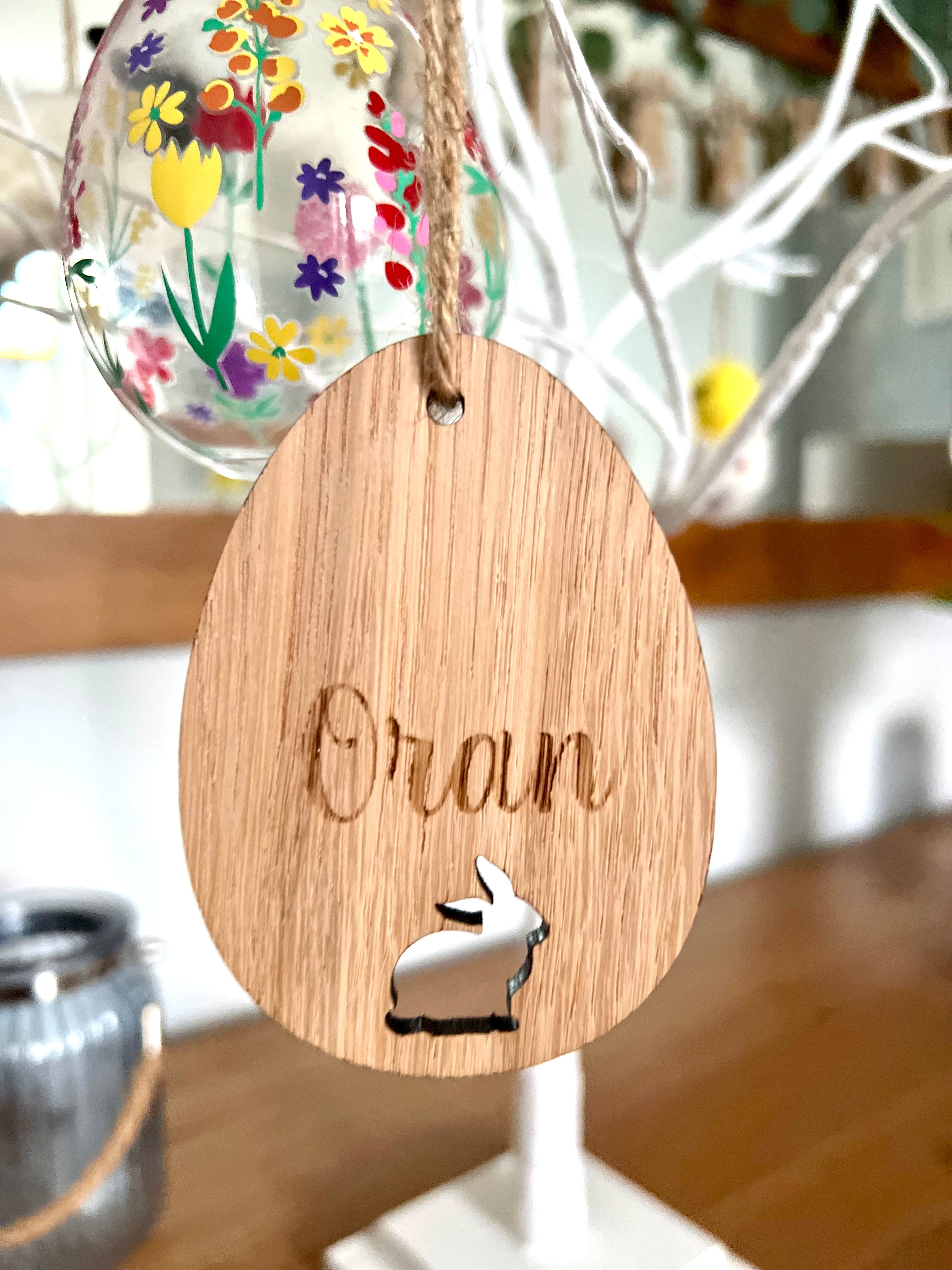 Load image into Gallery viewer, A wooden hanging decoration featuring the word 'ORLA' carved in a bunny shape, with a colorful Easter egg behind it.
