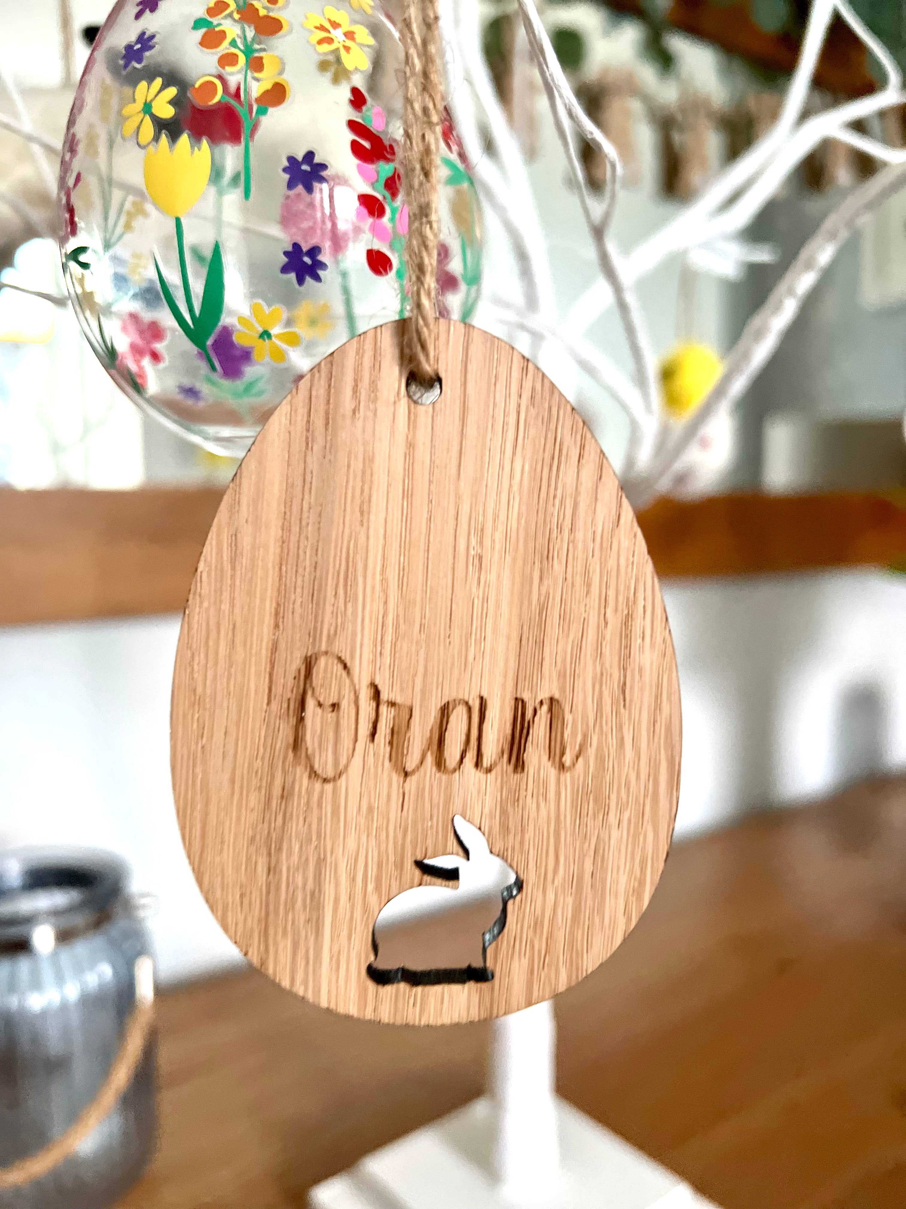 A wooden hanging decoration featuring the word 'ORLA' carved in a bunny shape, with a colorful Easter egg behind it.