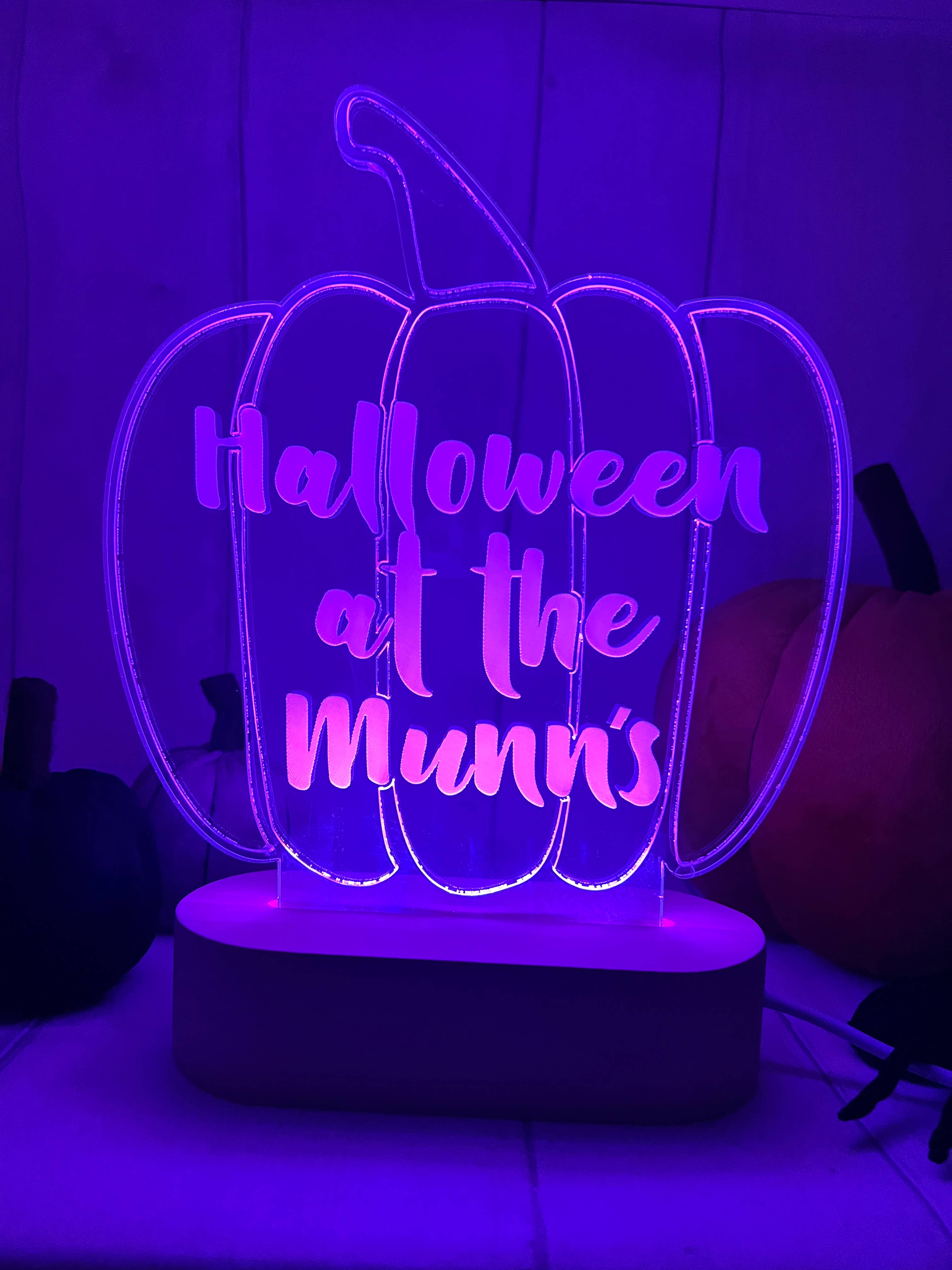 A personalised LED light up stand with a pumpkin shape, illuminated in purple and with the text 'HALLOWEEN AT THE MINNS' engraved on it.